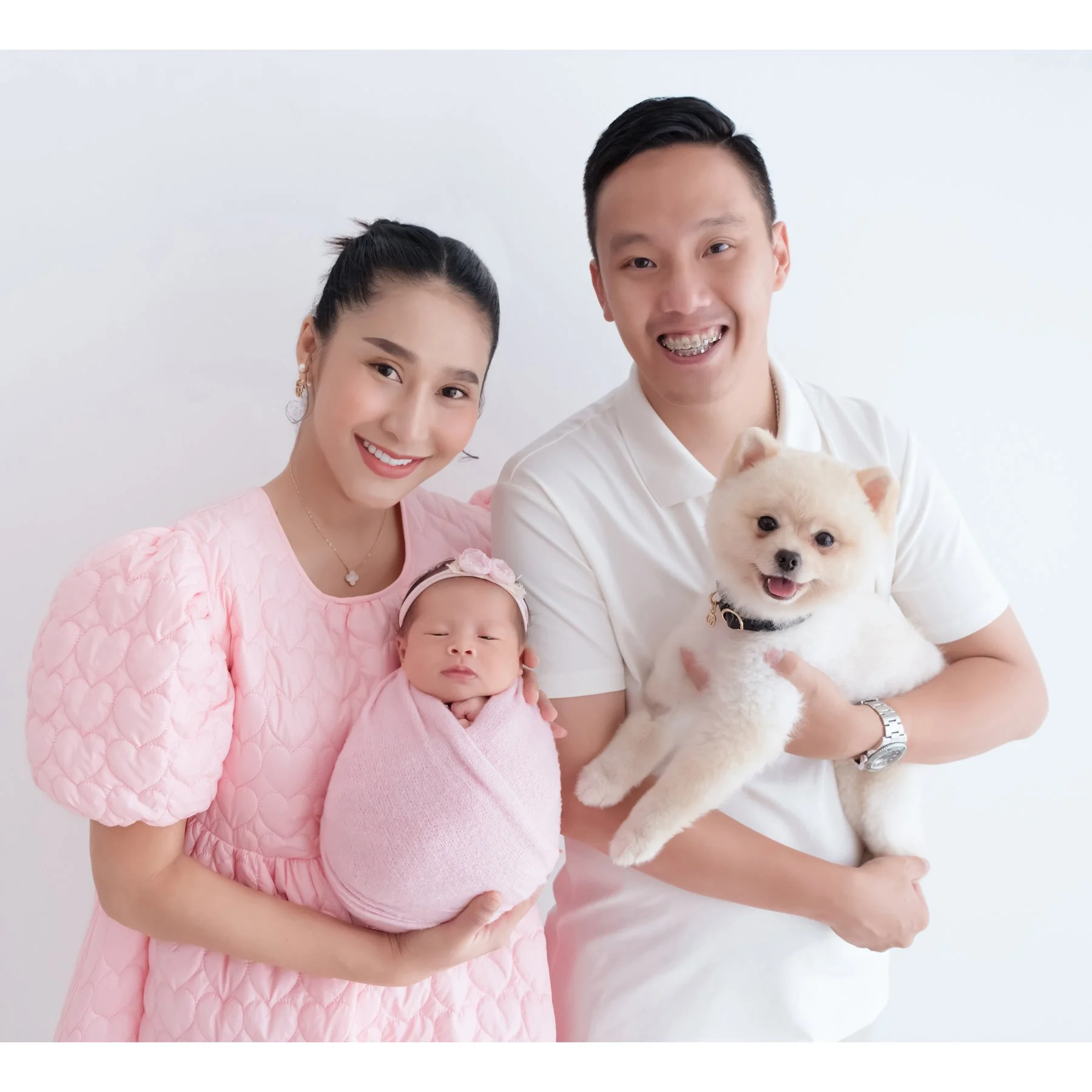 Smiling parents posing with their newborn in pink and their small white dog