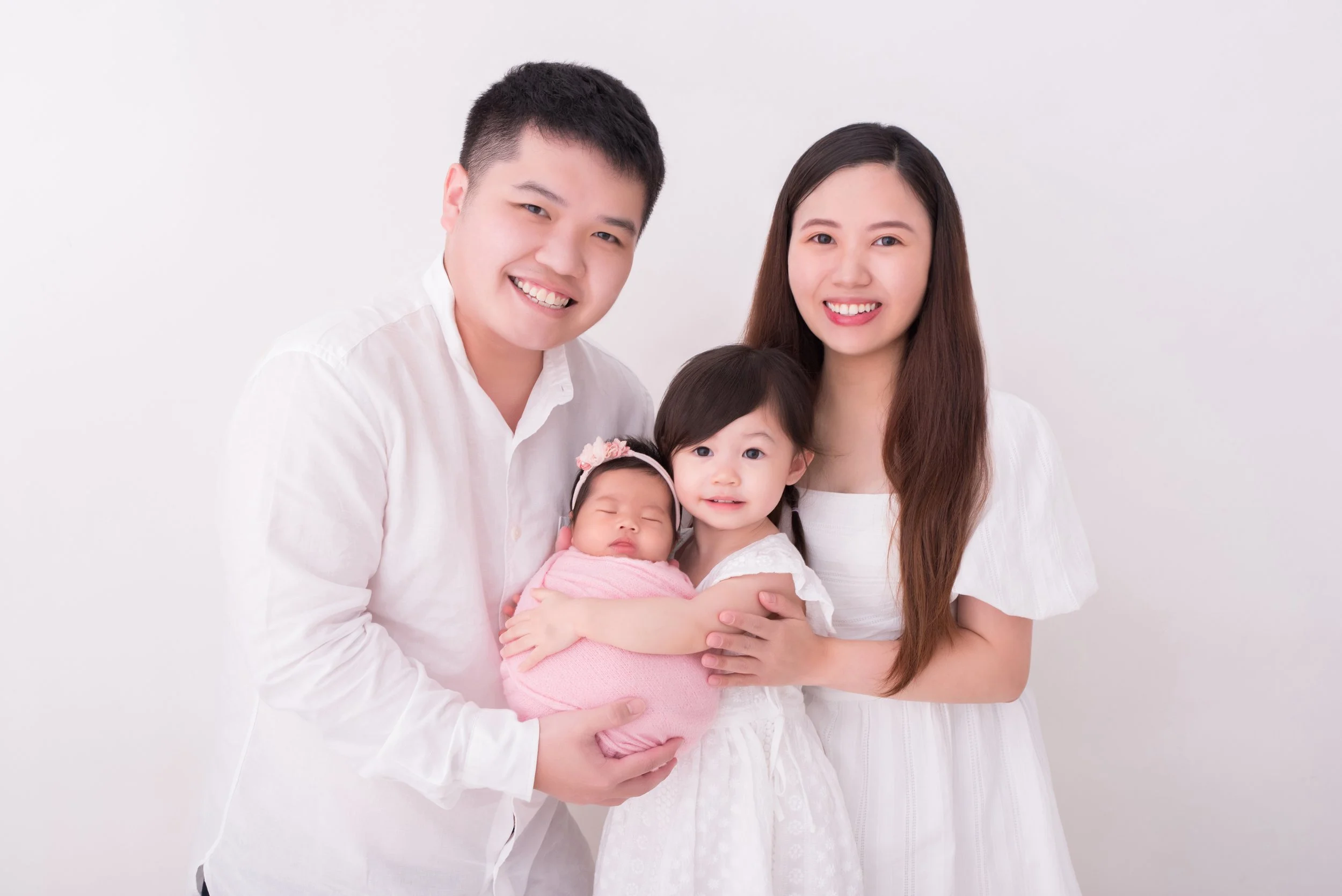 Parents and older sister smiling together with a newborn wrapped in pink