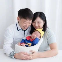 Parents gazing at their newborn dressed in a blue and red Superman outfit