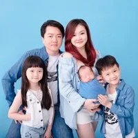Family of five posing with their newborn wrapped in blue against a blue backdrop