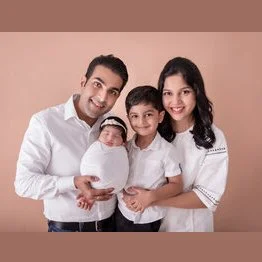 Parents and older brother in white shirts holding a newborn wrapped in white