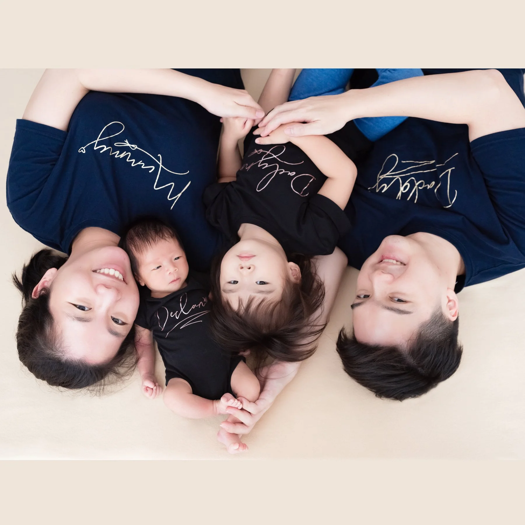 Parents in black lying beside their newborn on a cream blanket, photographed from above