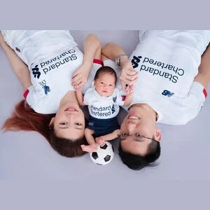 Parents and newborn wearing matching white football shirts beside a miniature football