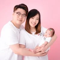 Smiling parents holding their newborn in white against a pink studio backdrop