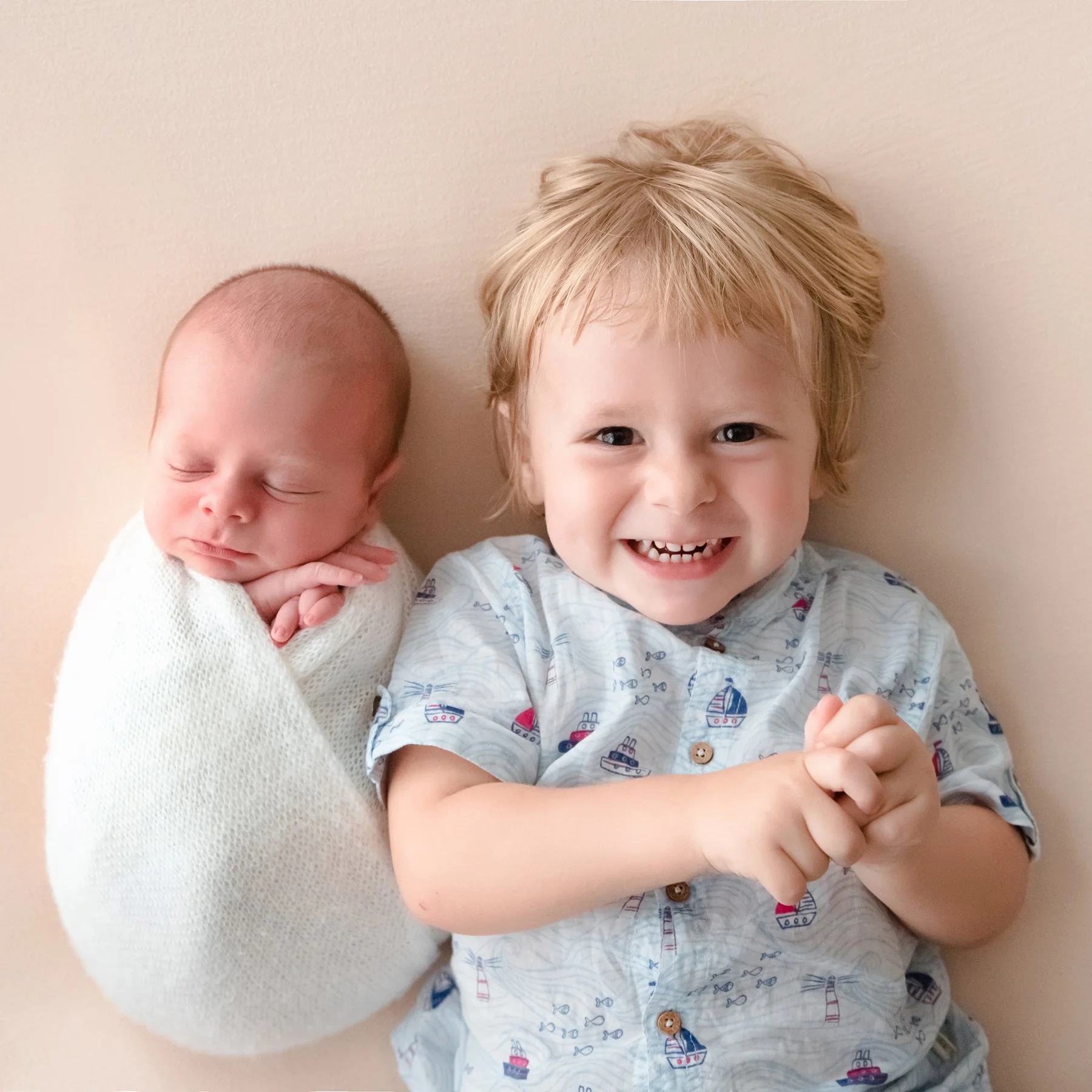 Smiling older sister lying beside her newborn sibling wrapped in white
