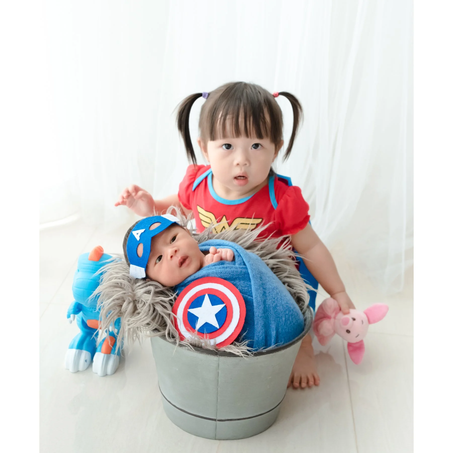 Older sister dressed as Wonder Woman beside her newborn sibling wrapped as Captain America