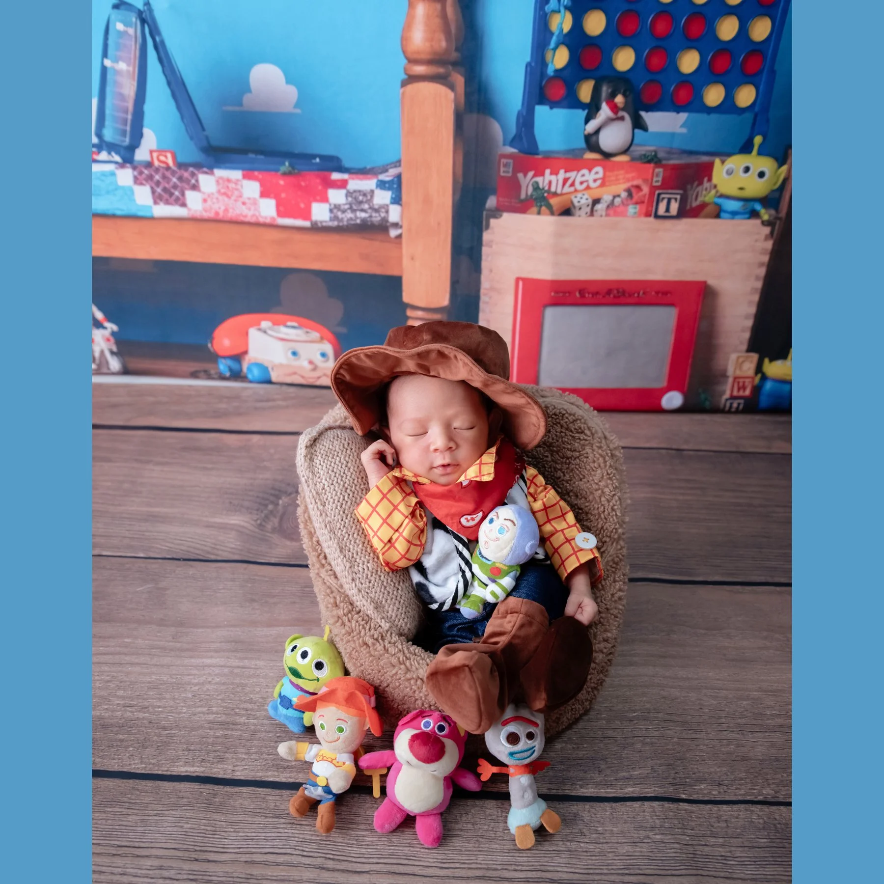 Sleeping newborn in a Woody outfit seated in a basket surrounded by Toy Story toys against a bedroom backdrop
