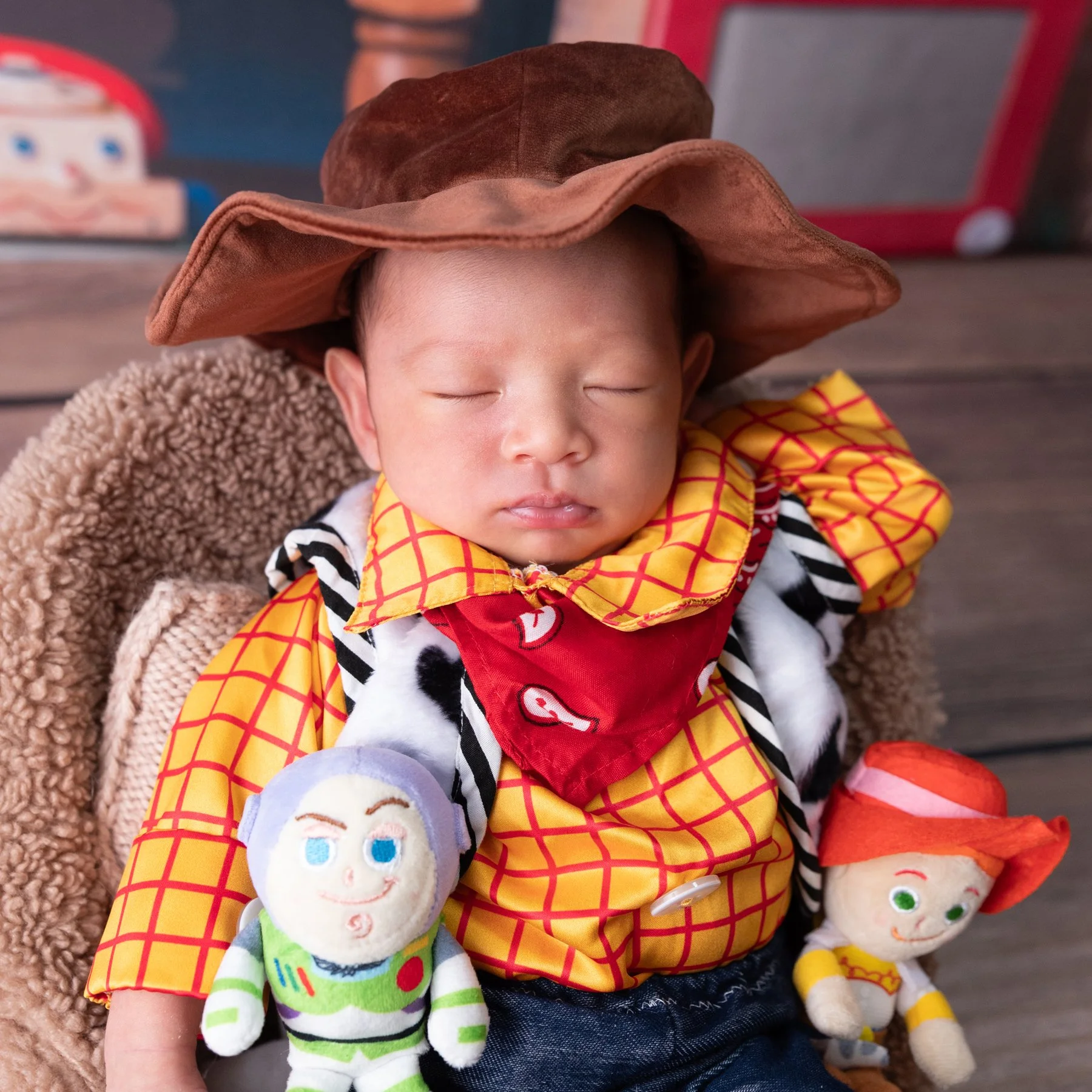 Close-up of a sleeping newborn in a brown cowboy hat and Woody shirt with Buzz Lightyear and Jessie toys