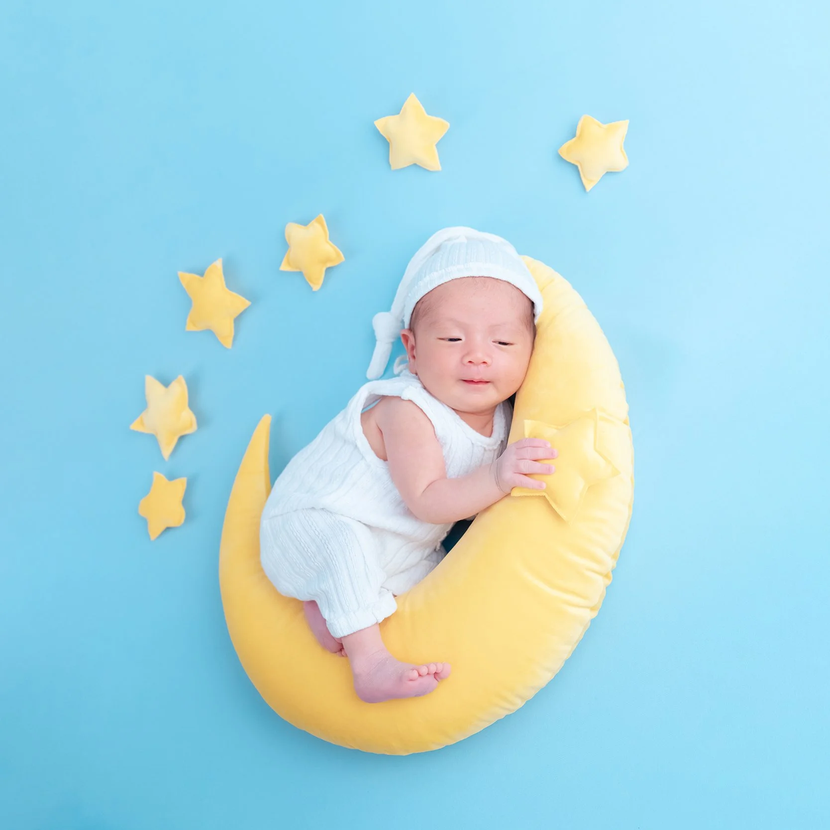 Sleeping newborn on a yellow crescent moon with stars against a blue backdrop