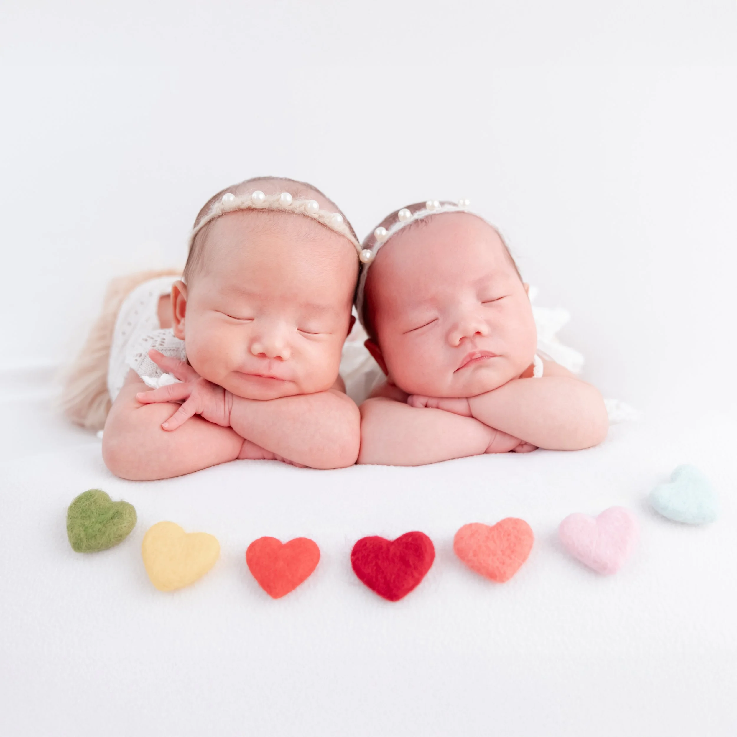 Sleeping newborn twins wearing floral headbands with their hands folded beneath their cheeks