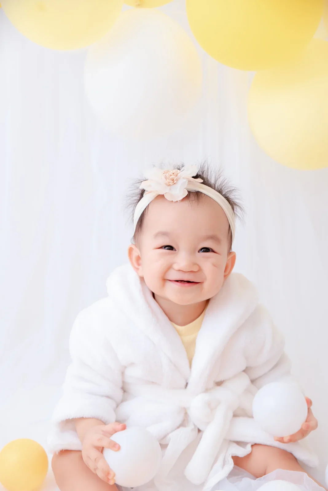 Smiling baby in a white bathrobe and floral headband photographed before digital background editing