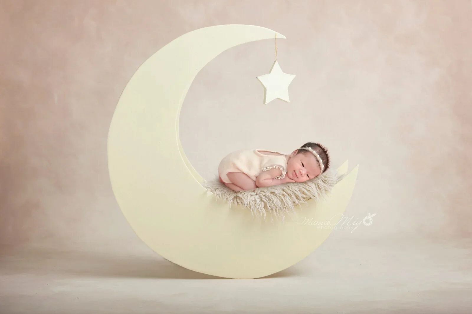 Sleeping newborn in a pink wrap resting on a digitally added crescent moon