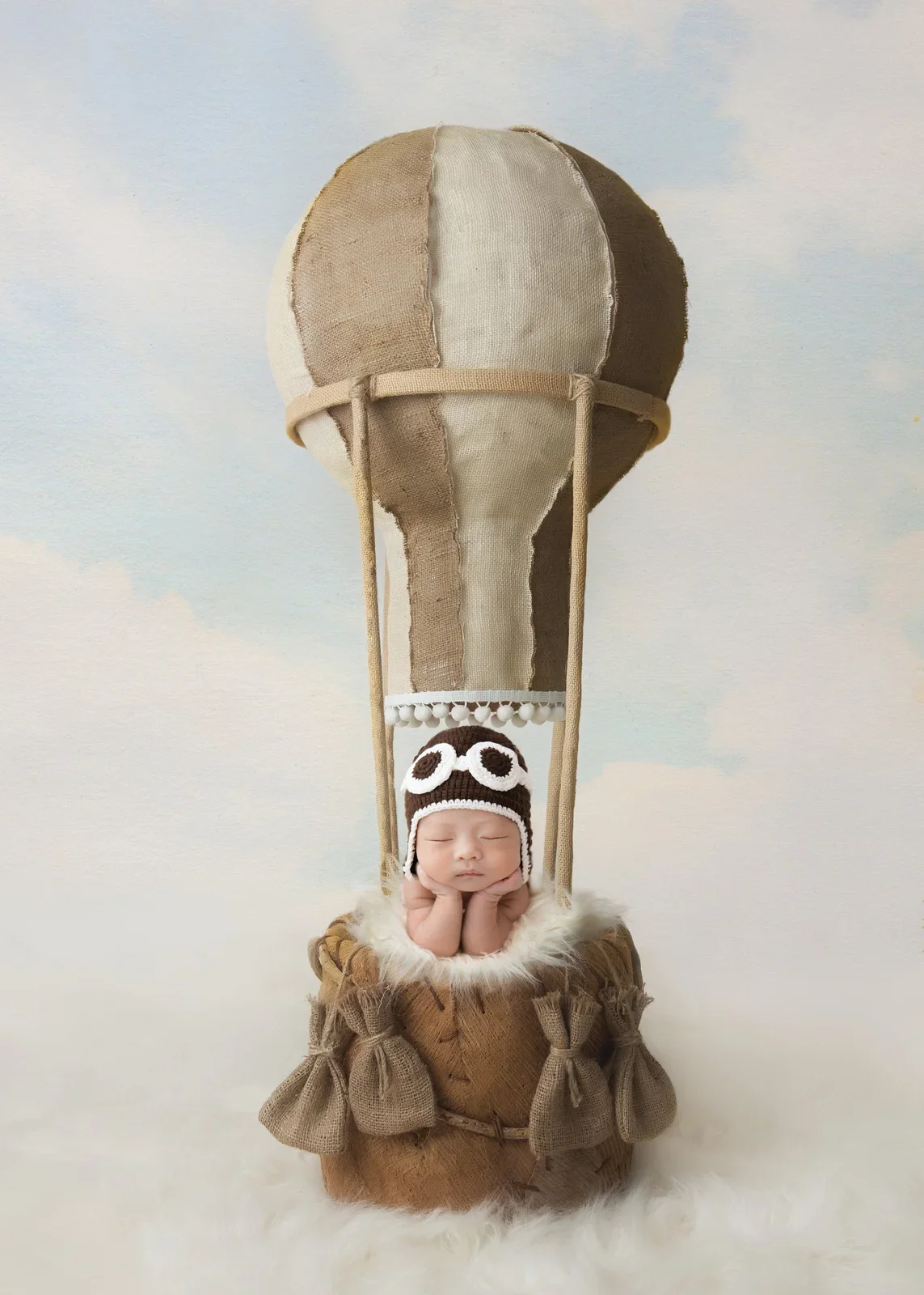 Sleeping newborn in an aviator outfit beneath a digitally added hot-air balloon
