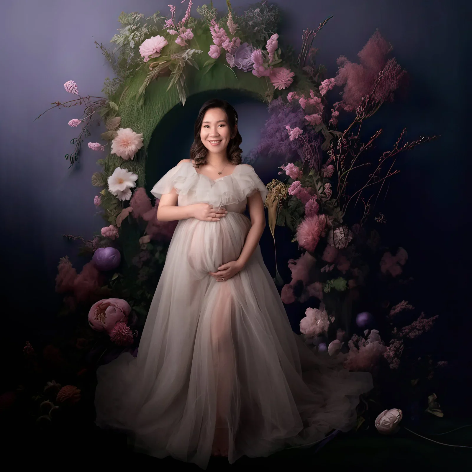 Expectant mother in a cream gown beneath a dark floral digital arch