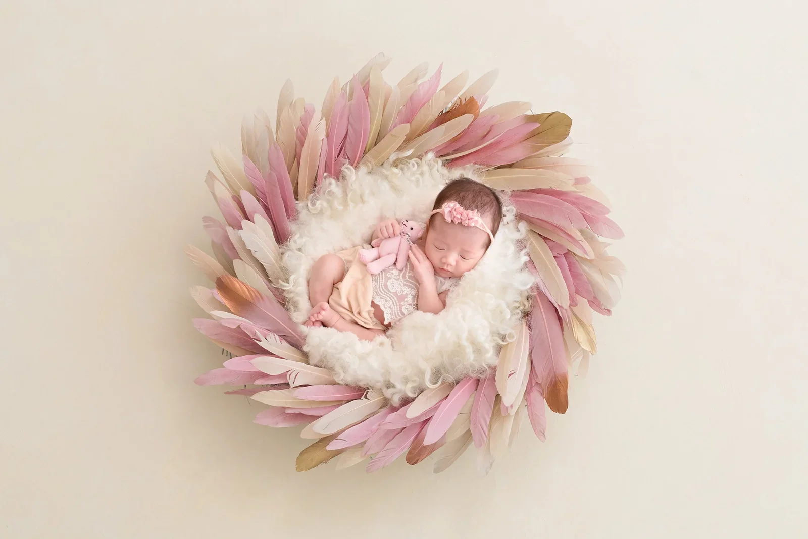 Newborn in a pink wrap surrounded by digitally arranged feathers