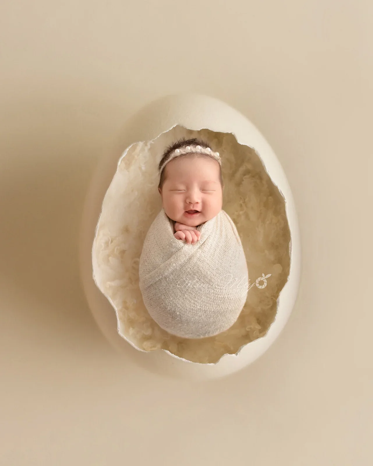 Sleeping newborn wrapped in white in an oval nest on a beige background