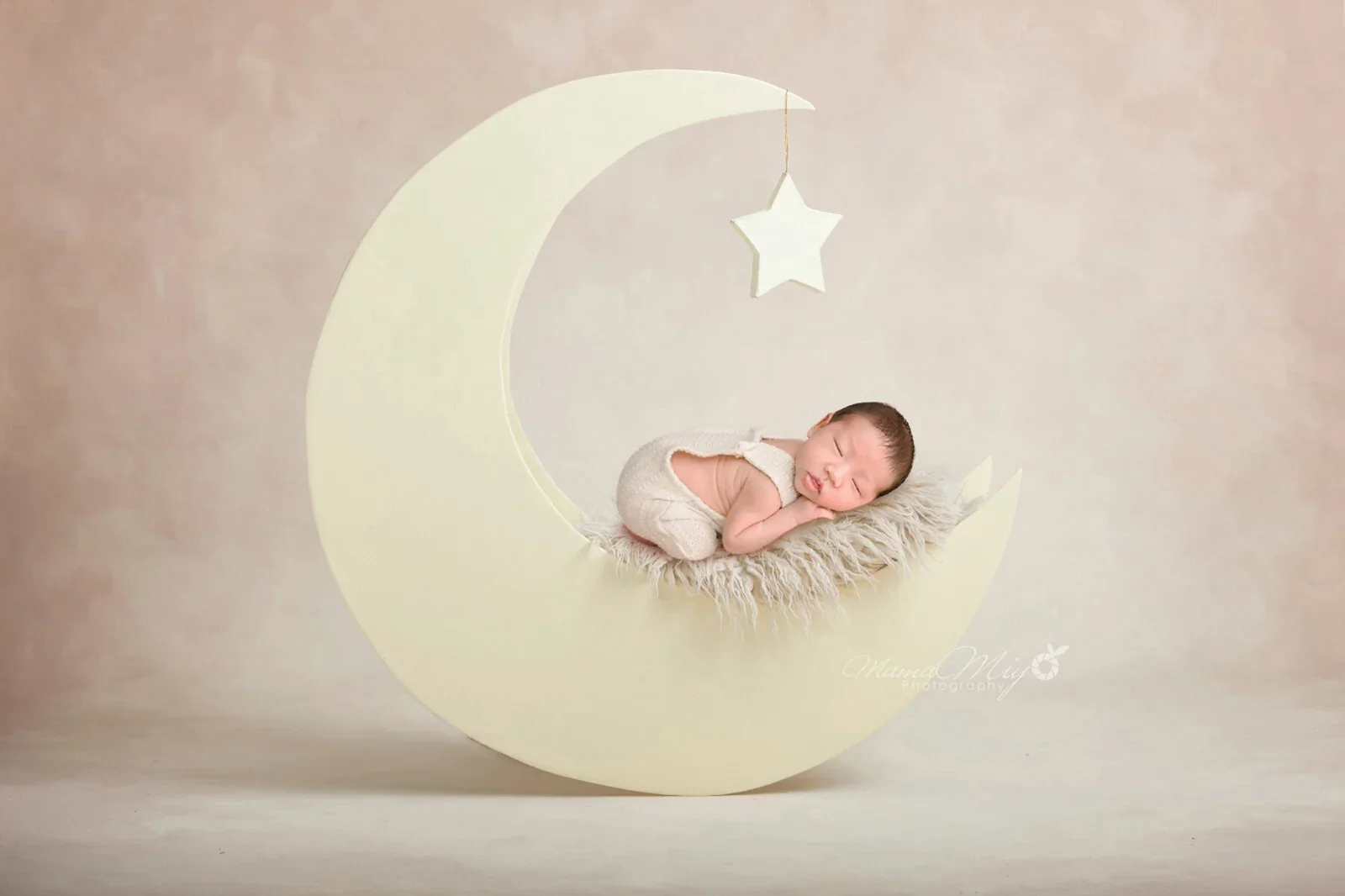 Sleeping newborn on a crescent moon prop beneath a hanging star