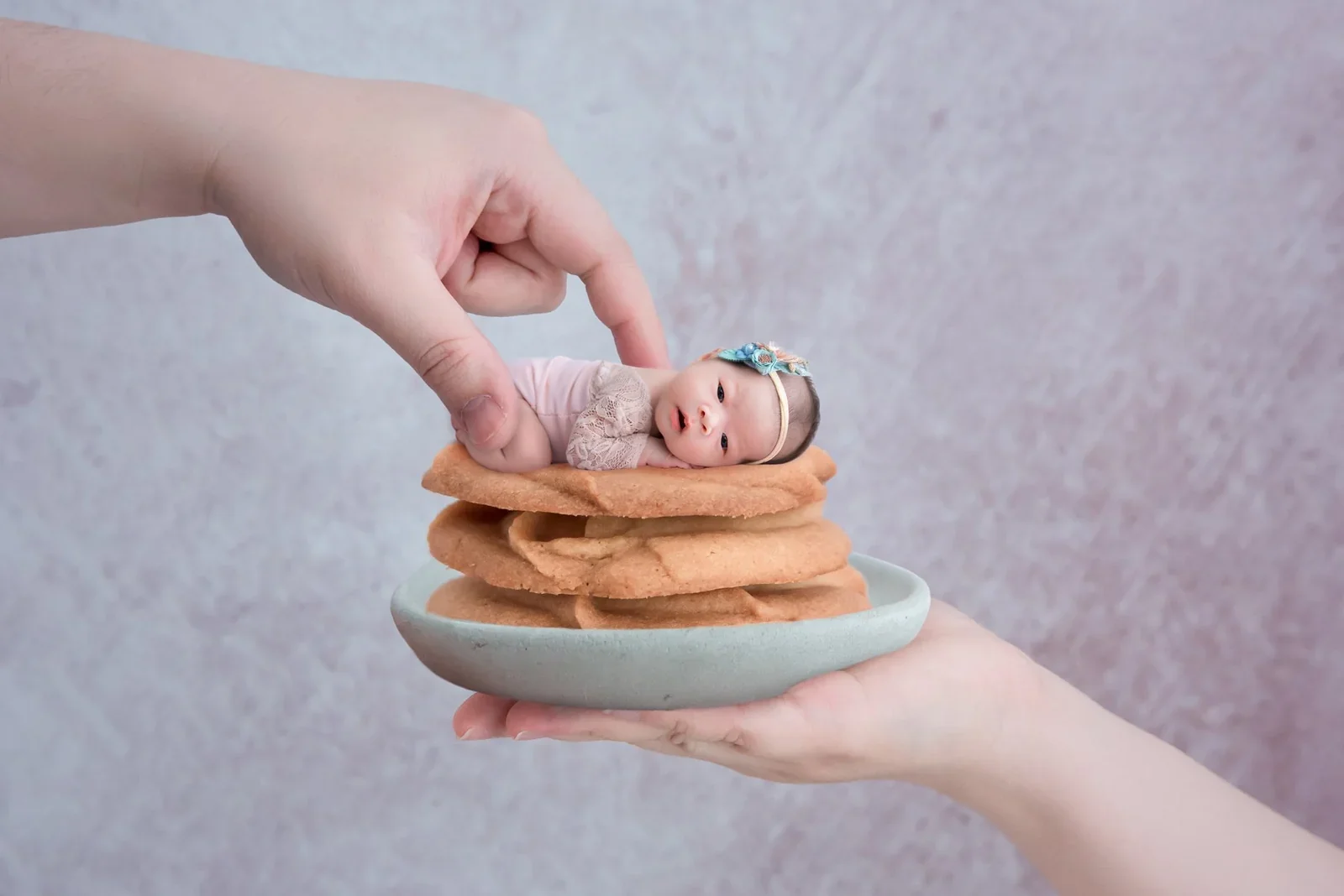 Miniature newborn resting on a stack of cookies on a plate held by a hand in a playful digital composition