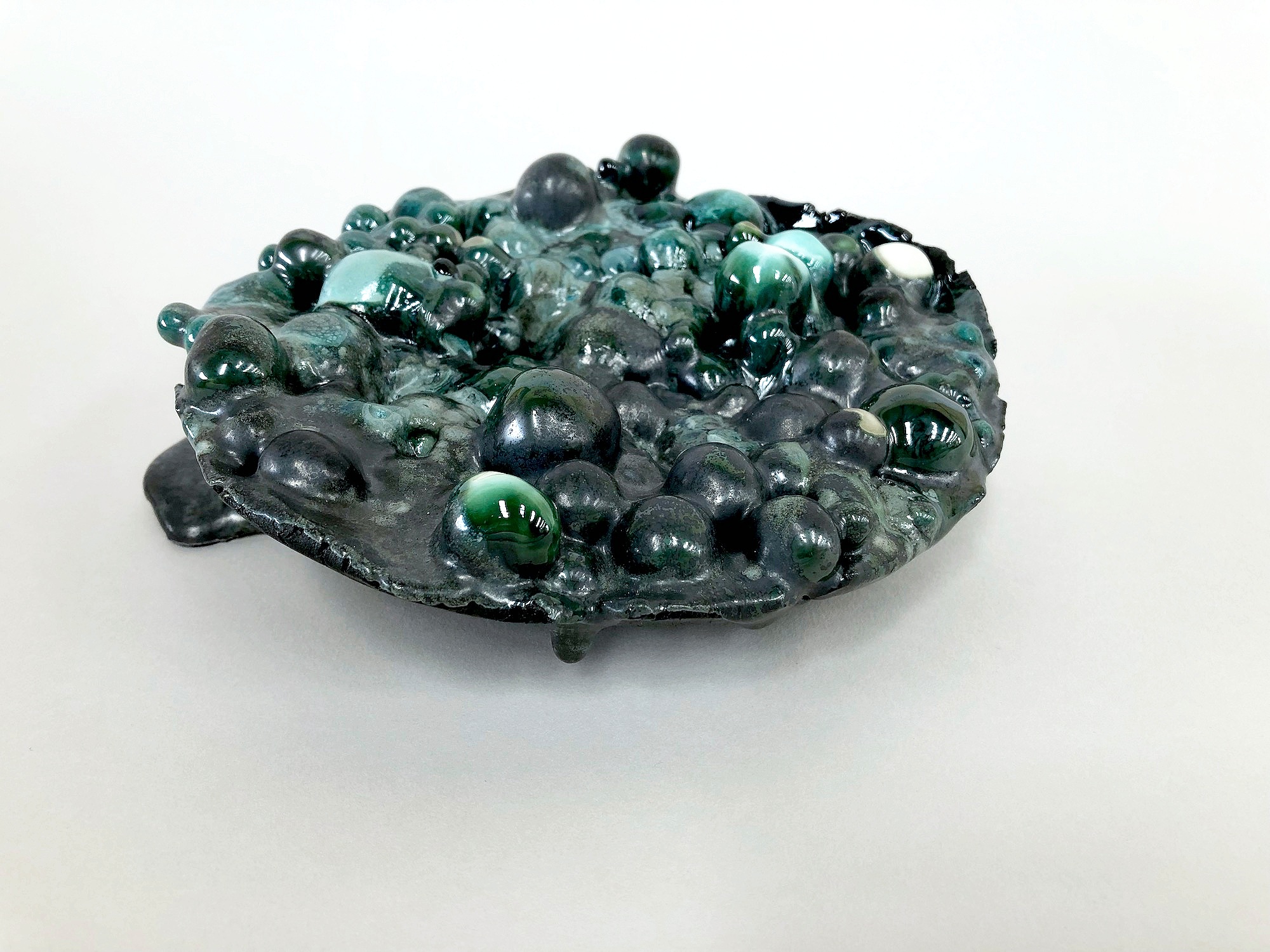 A callout was made by ANU and Geoscience Australia for artists to respond to the specimens in the Geoscience collection. Botryoidal malachite specimens provided inspiration to assemble a series of ceramic elements using only copper carbonate as the colourant. Tests were conducted using different concentrations of copper carbonate in glazes, slips and porcelain. I used porcelain because it is considered the ‘purest’ of clays and the slip I used was also porcelain, the glazes were of the simplest formula I could make to ensure that the copper carbonate was the feature for colour and characteristic. A rough vessel was formed from intensely copper carbonate stained porcelain and porcelain spheres (stained with varying degrees of copper carbonate), dipped in copper stained glazes and slips were deposited within the vessel. This experimental work was then fired in an electric kiln, leaving the result to chance and is presented as Malachite Transformation .