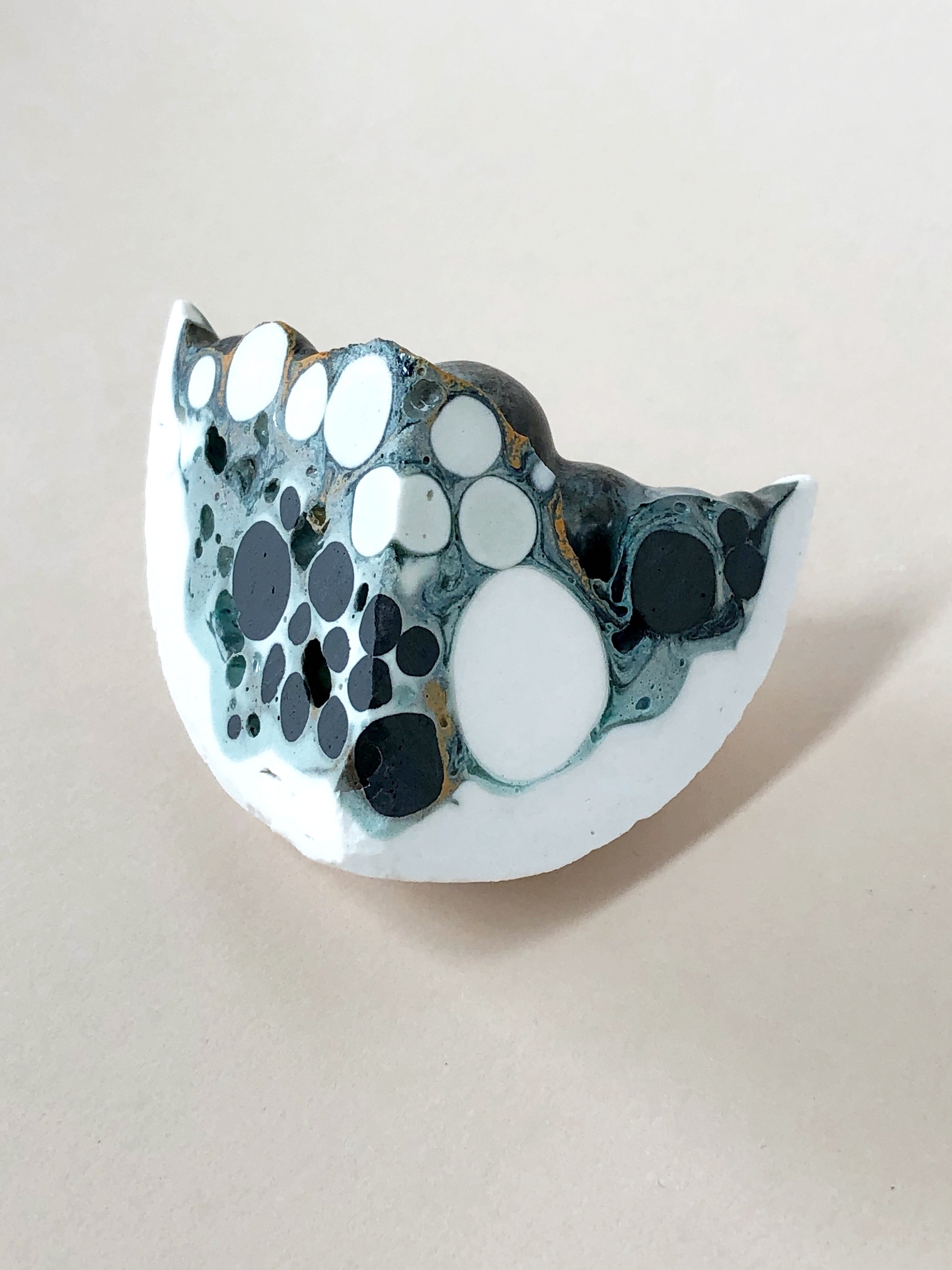 The work gives an impression of the variety of the possible states of matter, caught in time – the directional flow of liquid around the porcelain spheres, the settling of the solid, impervious spheres by gravity, the containment tendencies of the vessel, the cooling of the boiling glaze catching internal bubbles in an attempt for the glaze to de-gas, the flux of the interior of the captured bubbles and the increased concentration of copper on the surface of the internal porcelain spheres. The differential tensions and pressures created by the tendencies and capacities (different coefficients of cooling/thermal expansion) of the individual components causing the whole to be compromised. There is energy embedded in this object.