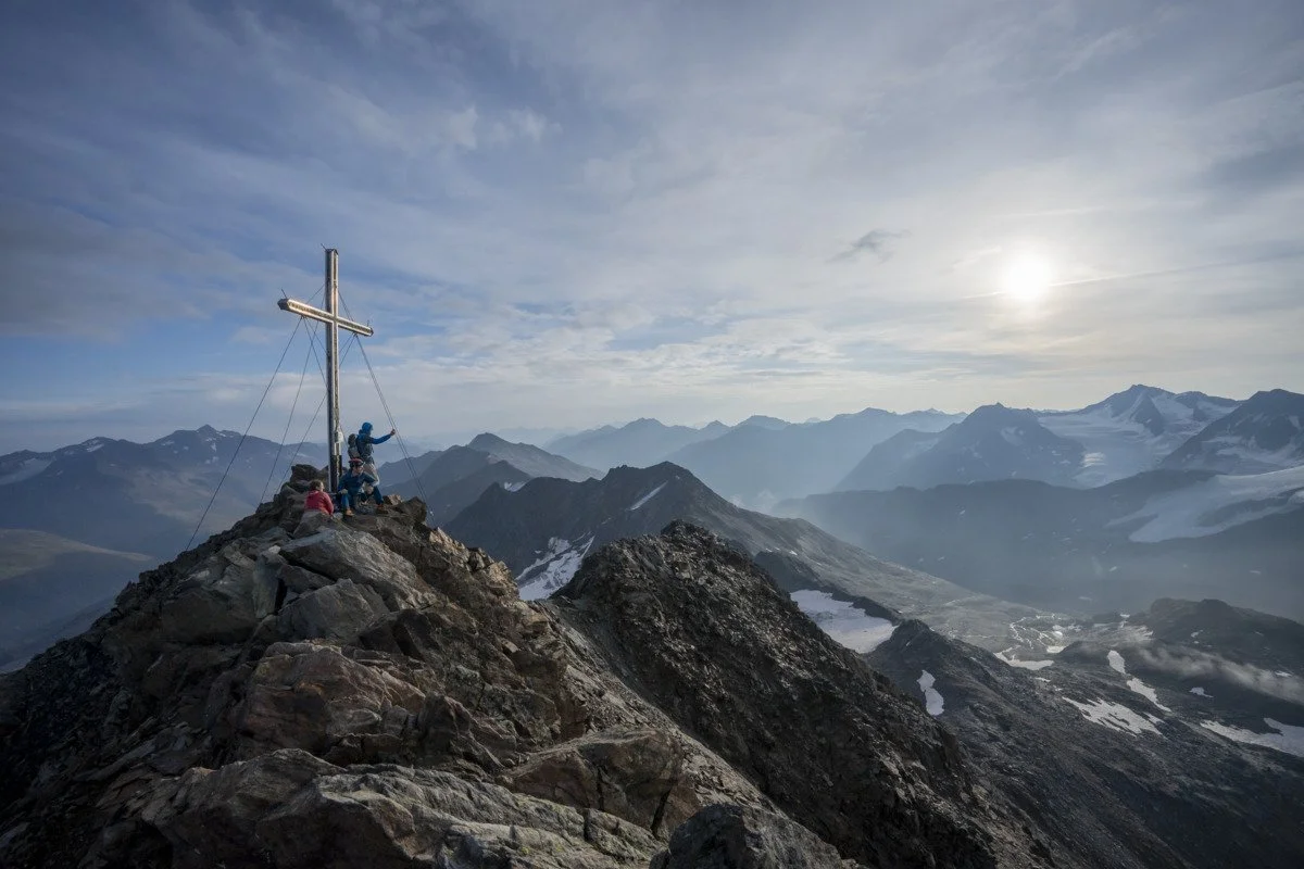 Zwei Bergsteiger am Gipfelkreuz der Finailspitze in den Ötztaler Alpen mit Blick auf die Gipfel in Südtirol.