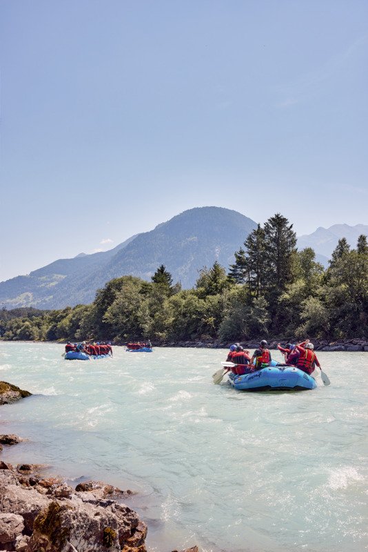 Mehrere Raftingboote auf dem Inn im Sonnenschein mit Blick auf den Haiminger Berg im Ötztal in Tirol.