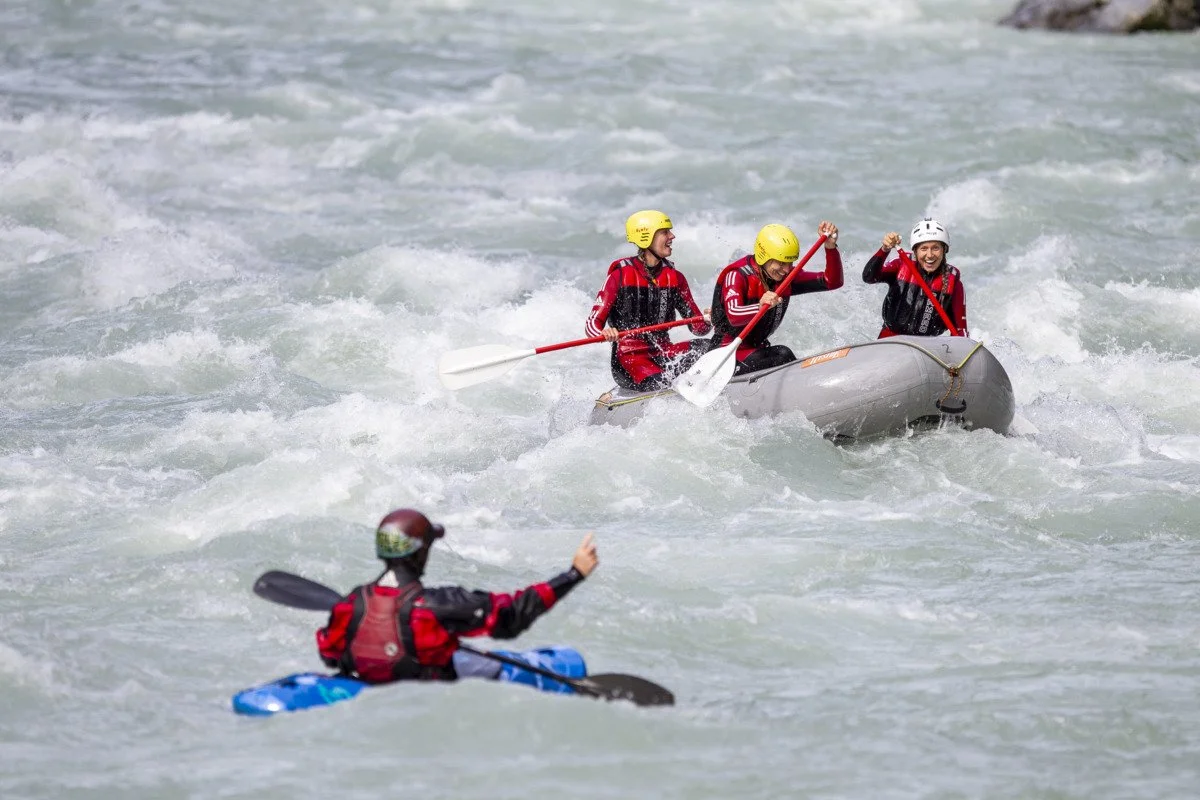 Ein Raftingboot und ein Kajakfahrer in aufgewühltem Wasser auf der Ötztaler Ache im Ötztal in Tirol.