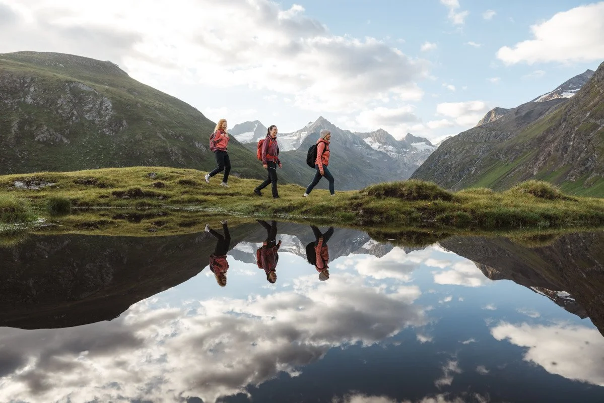 Drei Wanderinnen spiegeln sich in einem kleinen Gebirgssee in der Nähe von Obergurgl im Ötztal.
