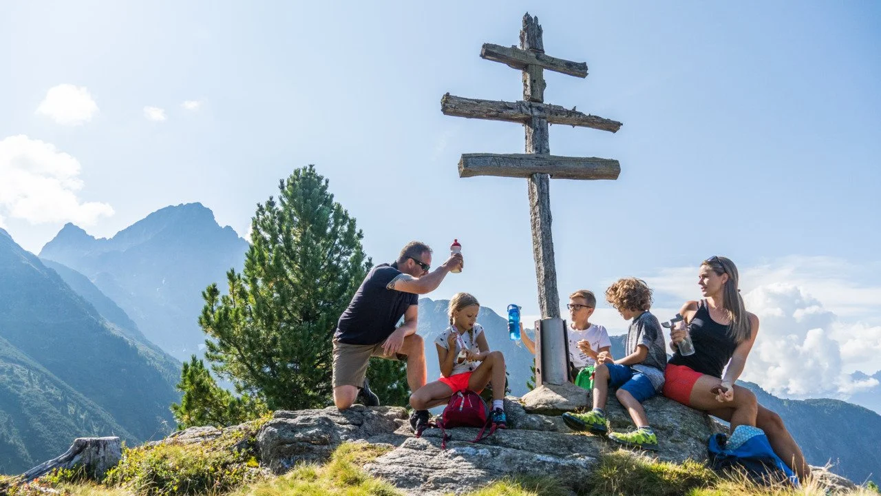 Eine Familie macht Jause am Gipfelkreuz in Hochoetz mit Blick auf die Berge im Ötztal in Tirol.