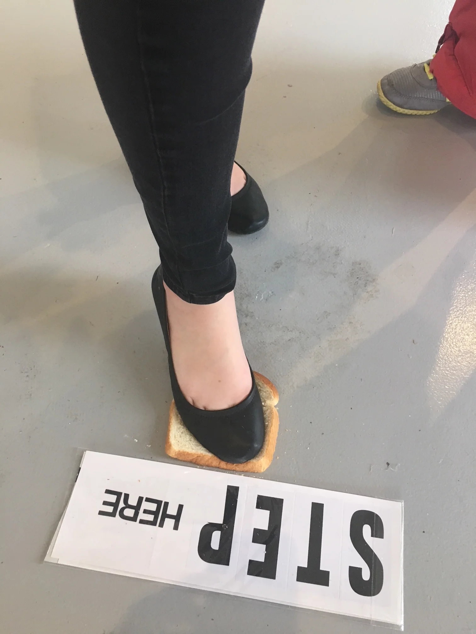 Workshop participants create a bread installation by stepping on wonder bread and leaving their shoe sole imprints on the bread. Bread is then hung on the wall with a nail.