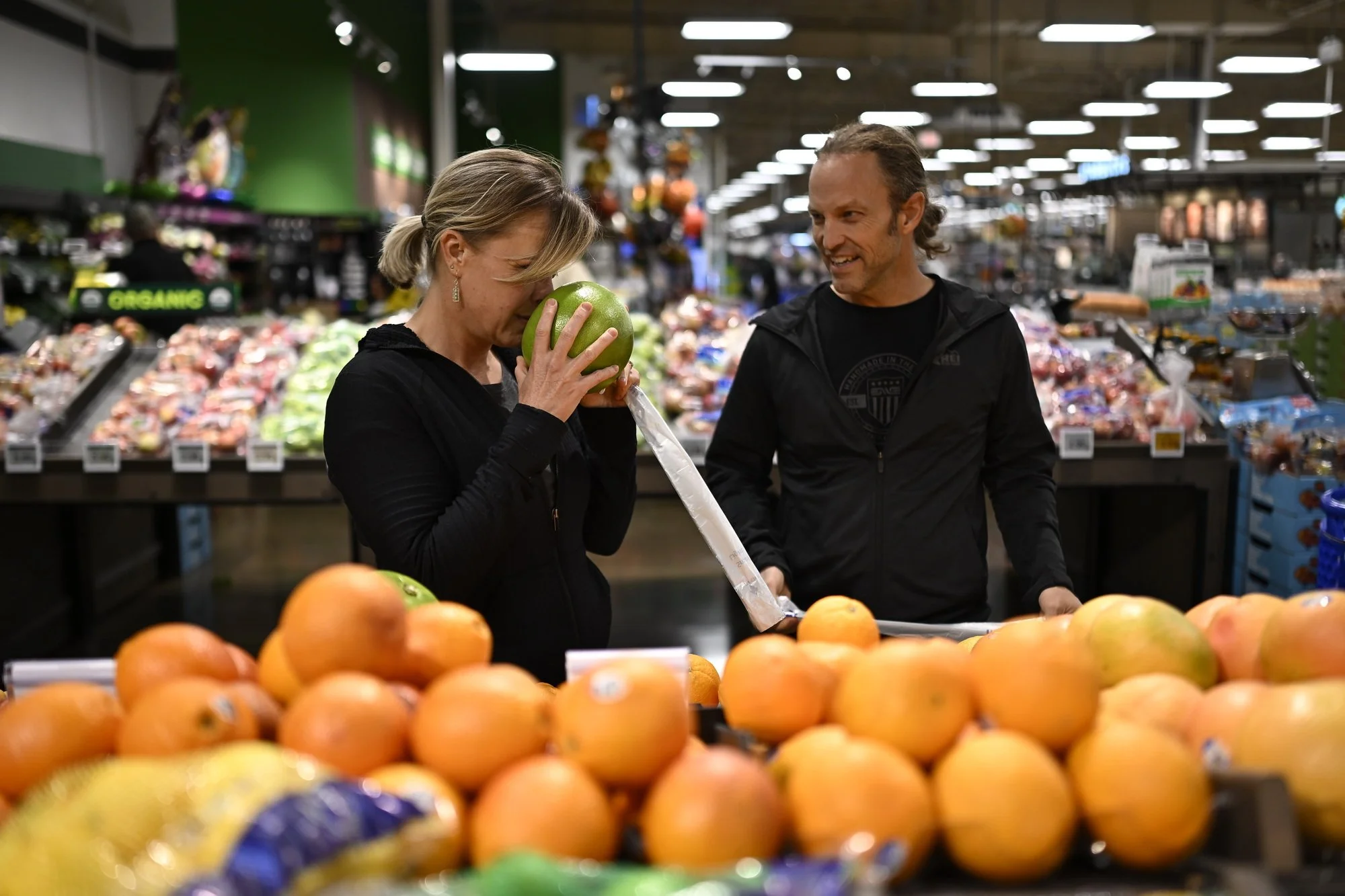  Christie Toffan, 47, smells a pomelo fruit  while shopping with her husband, John Meng, 46. The couple's nature-loving lifestyle extends to their focus on fresh produce and overall well-being. 