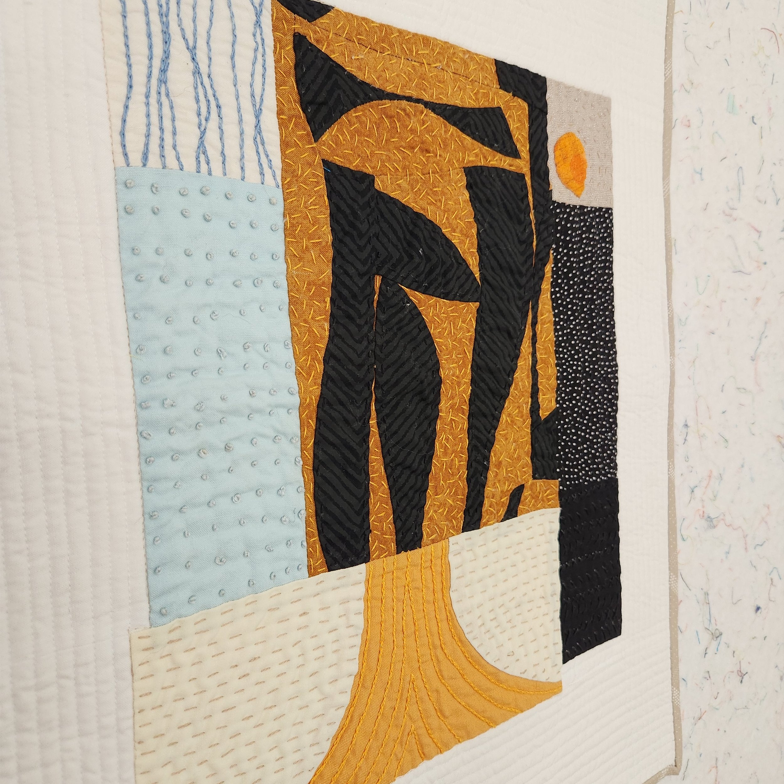 Hand embroidery and quilting details on a gold, black, and blue improv quilt
