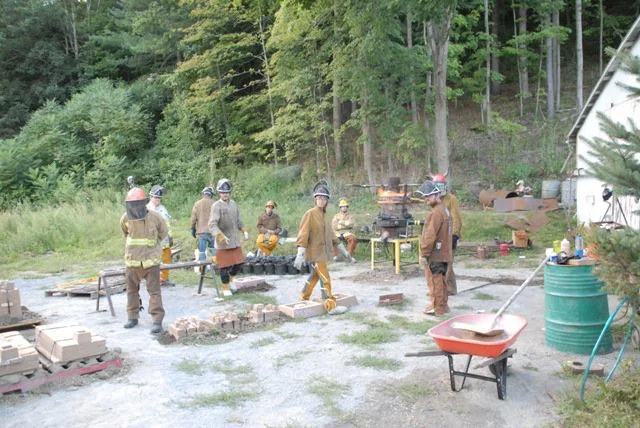 Pour Participants putting on their protective gear as well as heating up the solid iron in the Cupola