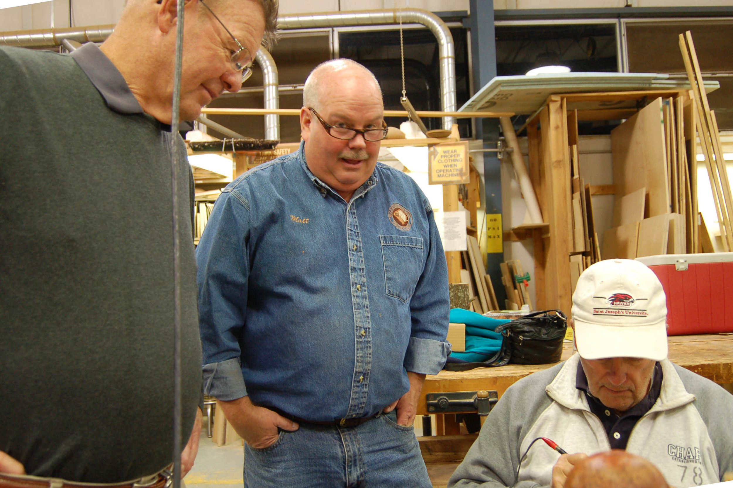  Keith Nelson and Matt Overton look on as John Williams demonstrates his signature pyrography. 