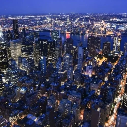 An aerial view of Manhattan at dusk with city lights shining brightly.