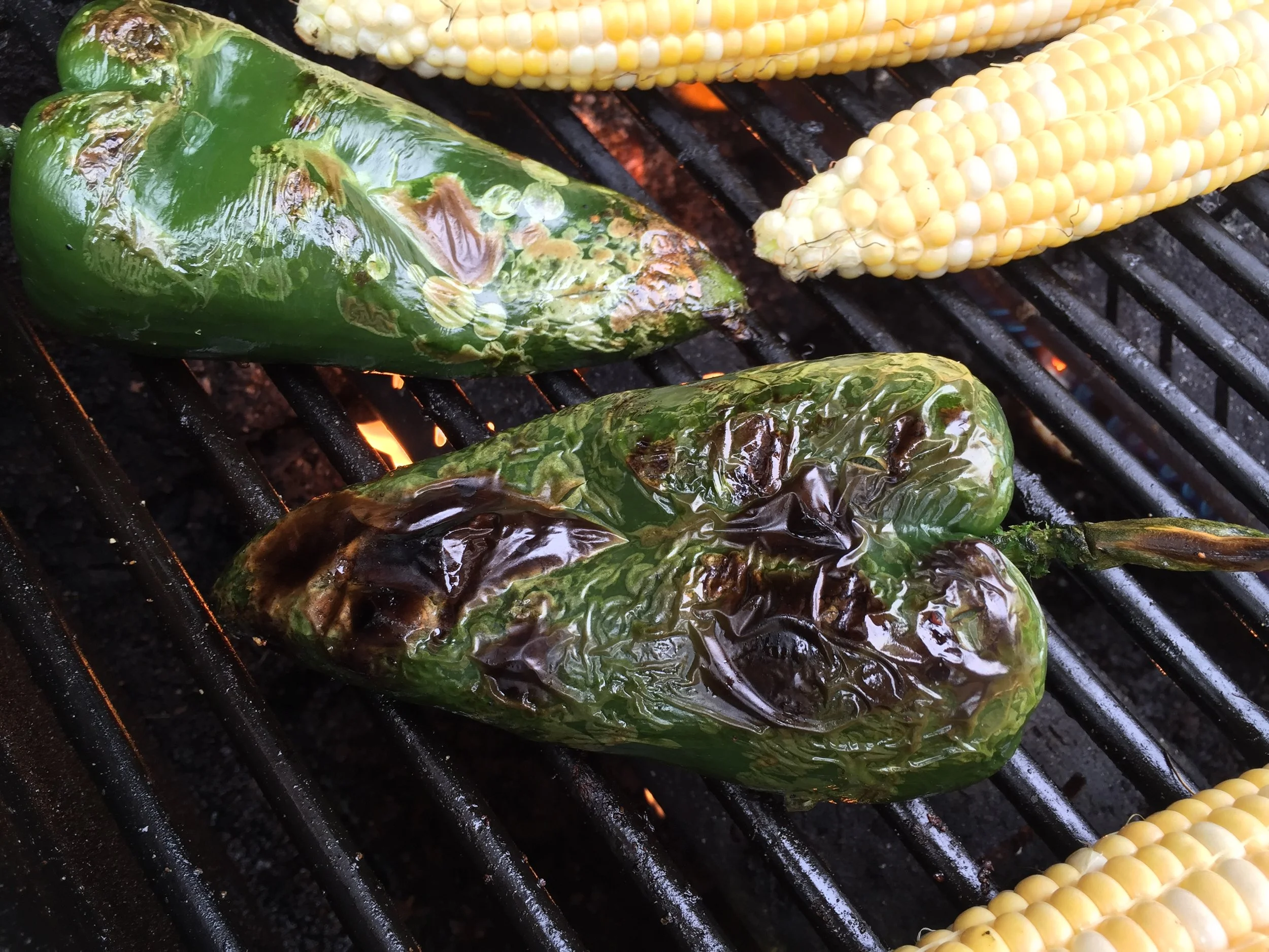 Poblano chiles roasting alongside ears of corn on the Adventure Kitchen grill.