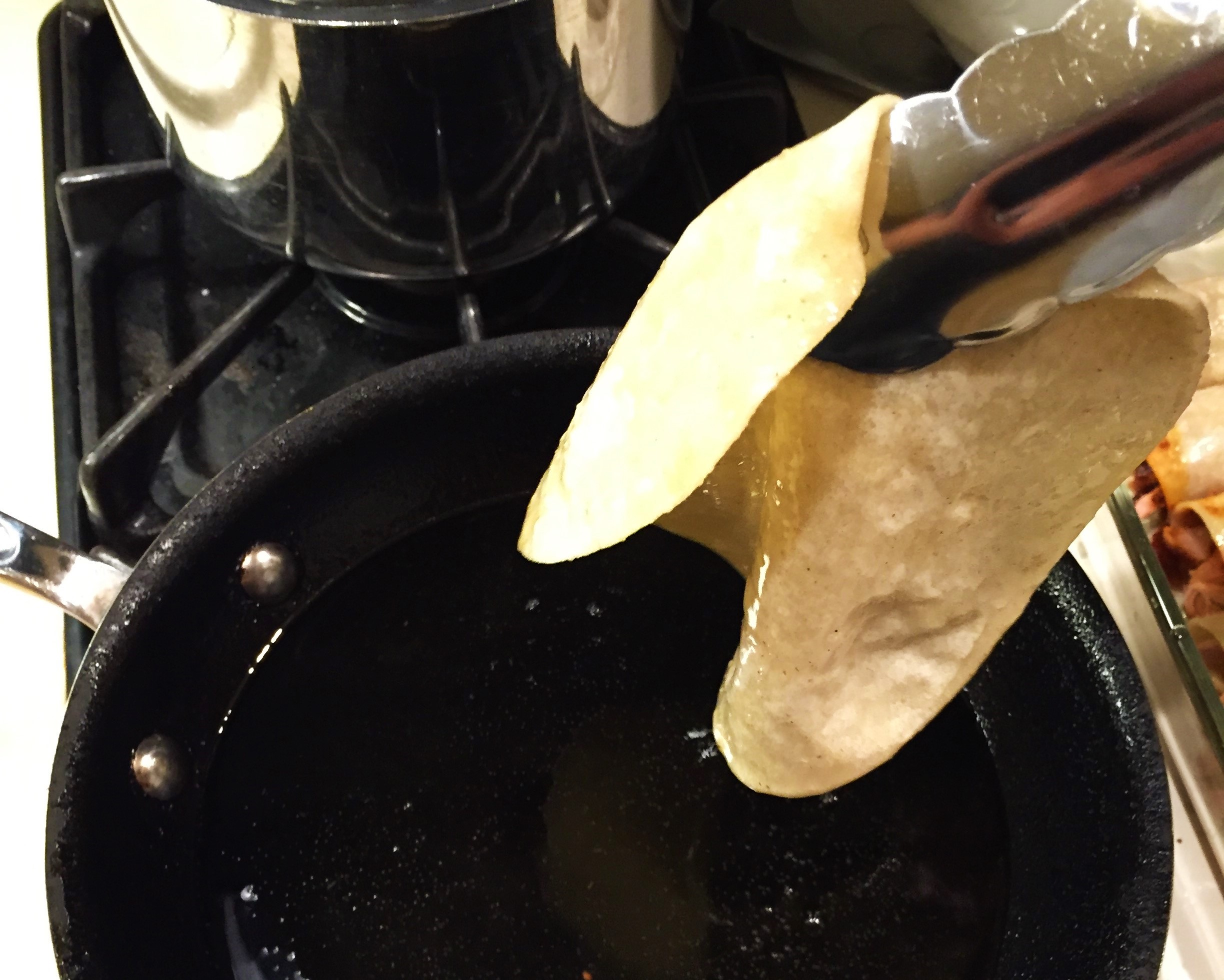 Removing the tortilla when it has softened in the oil, but before it becomes crisp