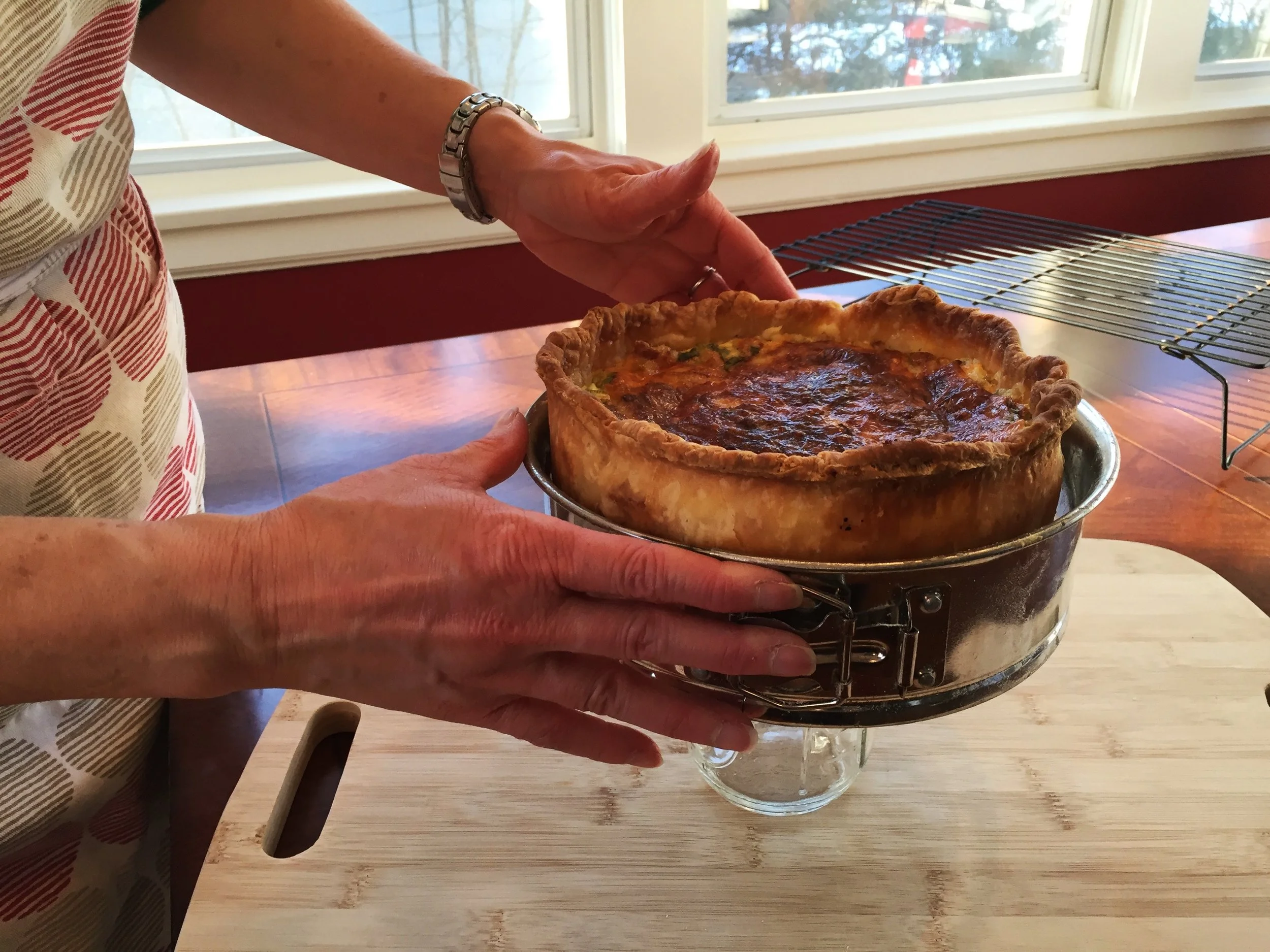 Removing quiche from springform pan. Pan is set on top of a jar, then the outer rim is loosened and slid downward, off of the quiche.
