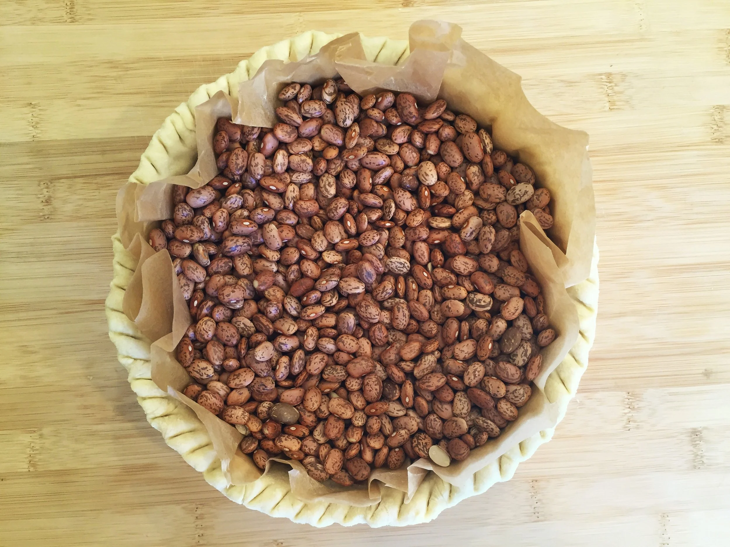 Beans are used as a weight to pre-bake a parchment-lined pie crust.