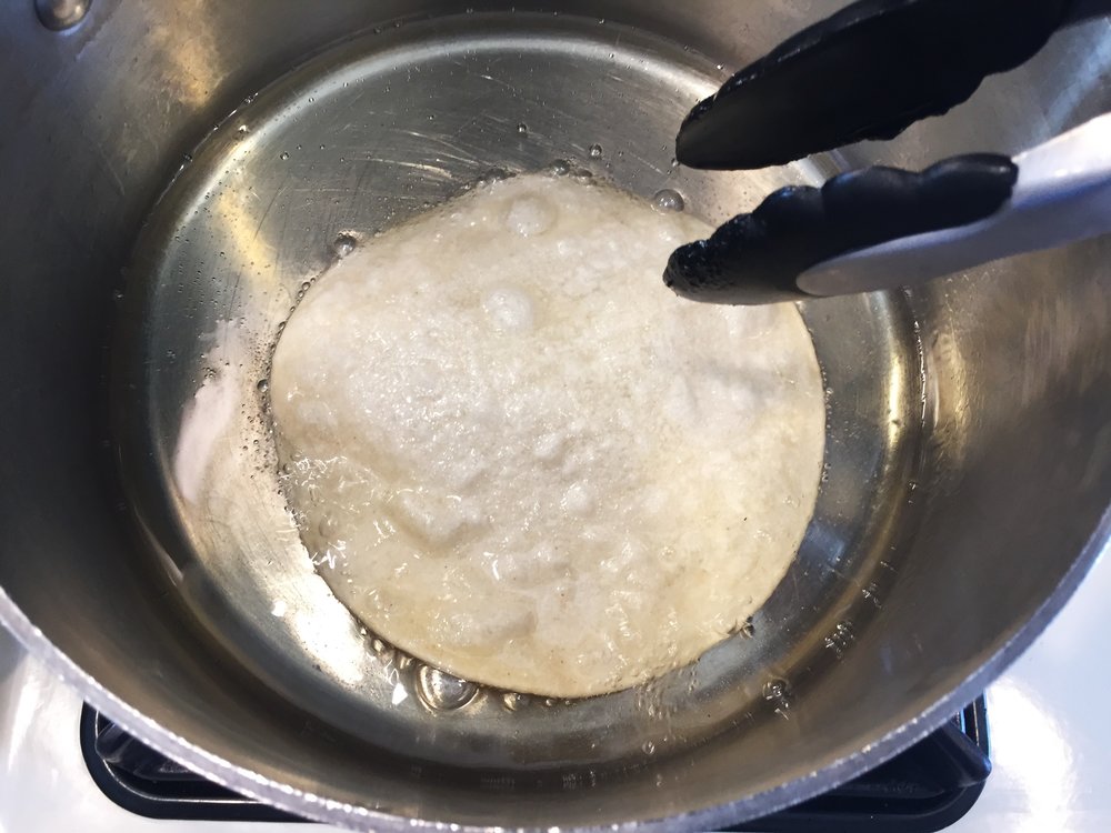 The tortilla begins to sizzle as soon as it touches the oil.
