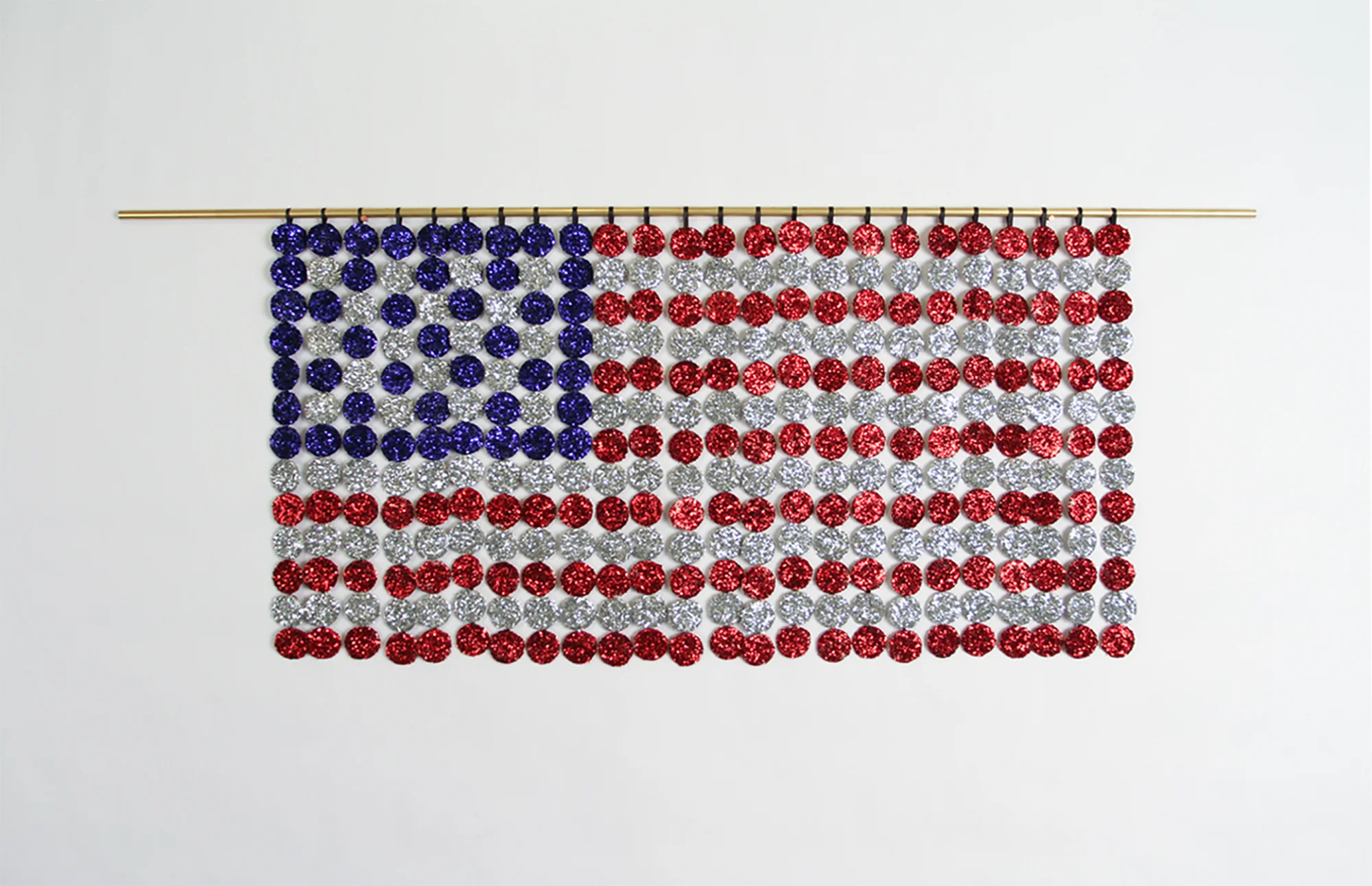Flag , 2017. Communion wafers covered in glitter, cotton, brass. 14.5” x 36” x .5”.