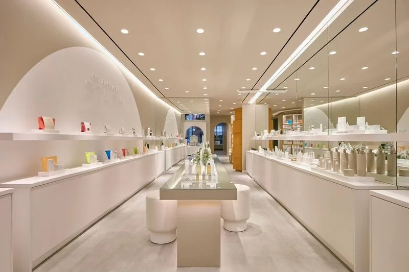 Modern beauty or skincare store interior with sleek white design, shelves displaying products, mirrors, and seating area.