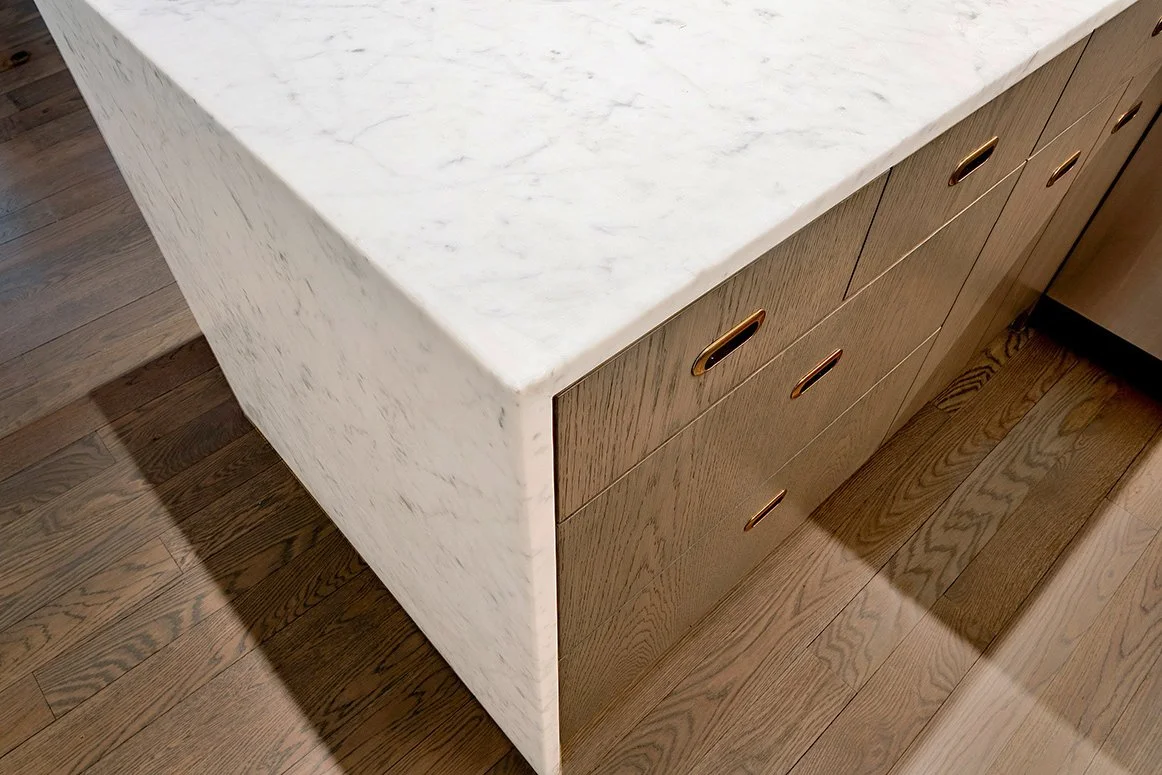 A white marble kitchen island with a wooden base and gold handles on the drawers, placed on a wooden floor.