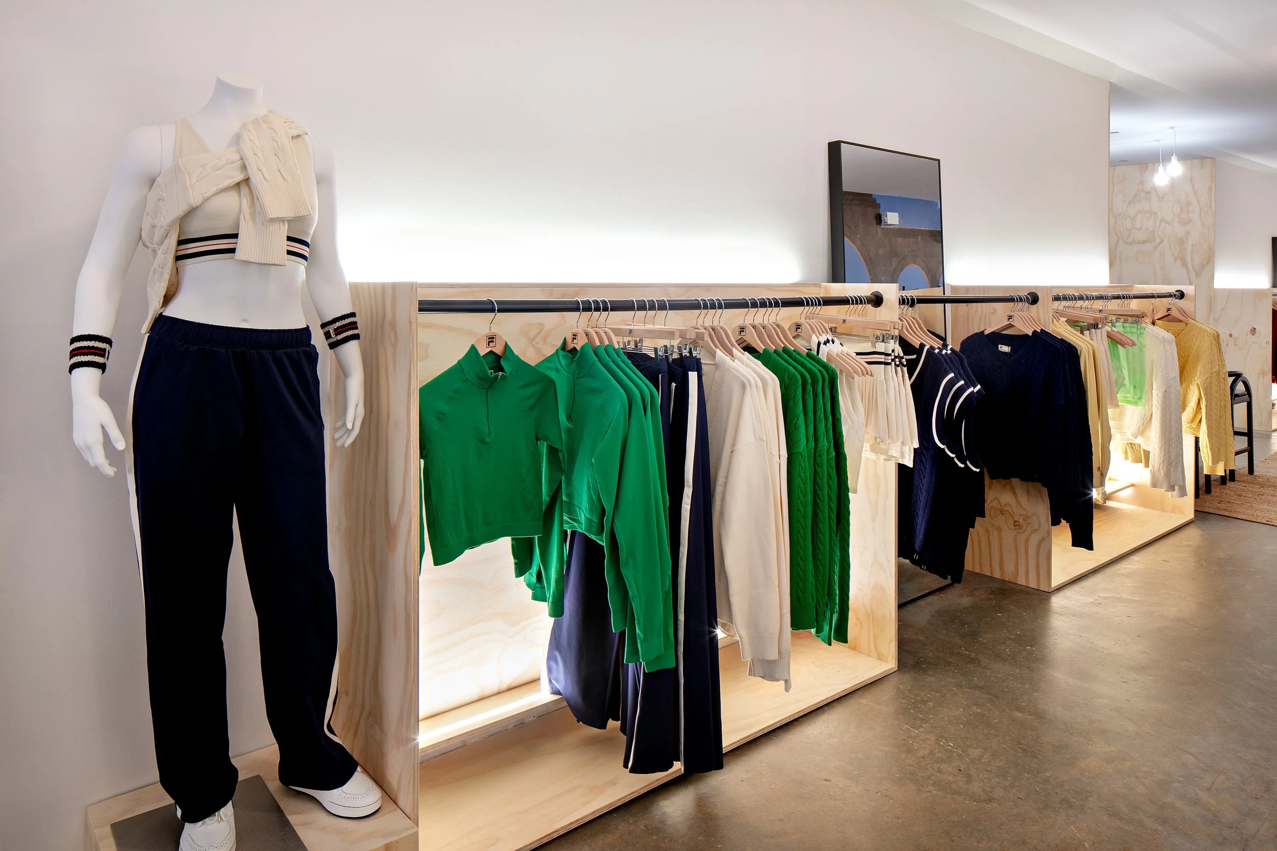 Clothing store interior with mannequin wearing athletic apparel and a rack displaying green, cream, and navy garments.