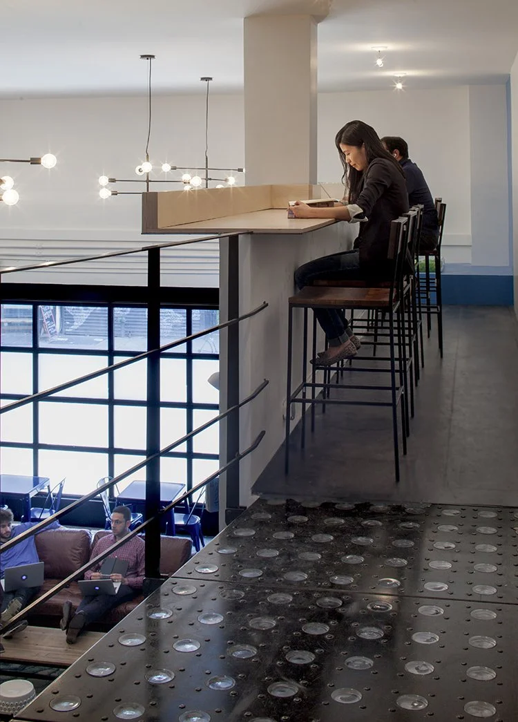 People working on laptops in a modern office with high stools and tables, and decorative lighting.