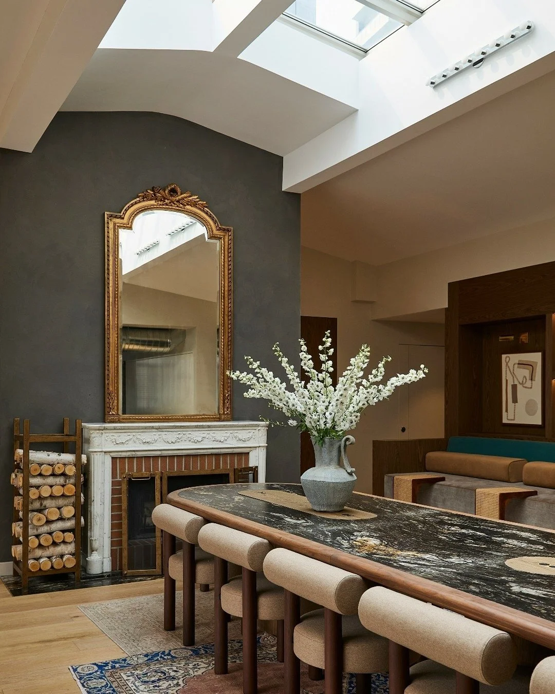 At the heart of our design for the SmartFlyer Penthouse, a striking 20-foot communal table anchors the space beside the original marble mantel fireplace and beneath the restored skylight&mdash;both preserved architectural features that lend character