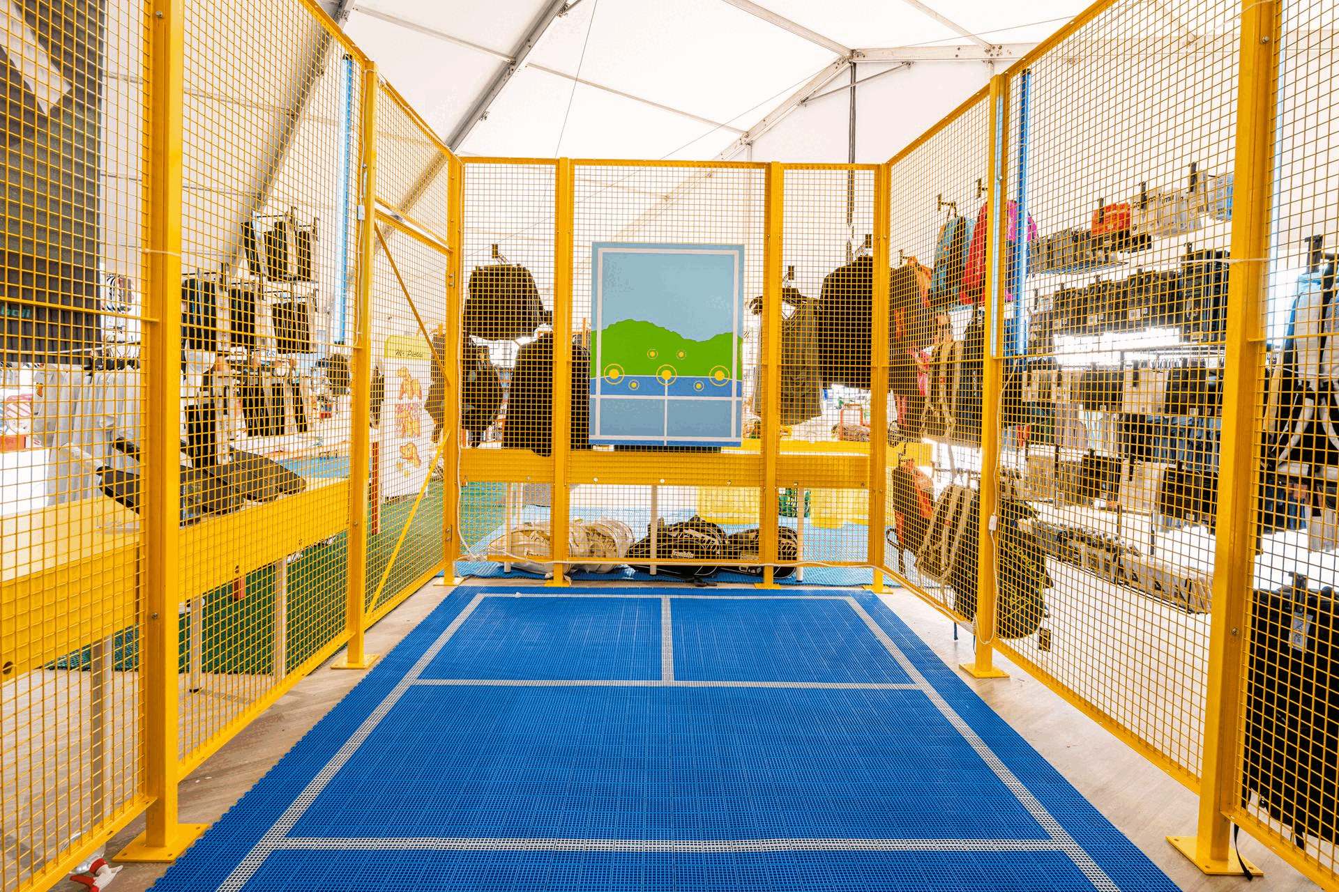 Fenced area in a retail store with backpacks displayed on yellow metal racks, blue flooring, and a landscape graphic on the back wall.