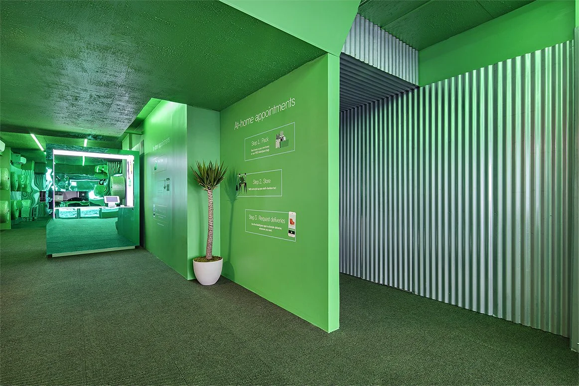 Modern green-themed interior with corrugated metal accents, potted plant, and text about at-home appointments on the wall.
