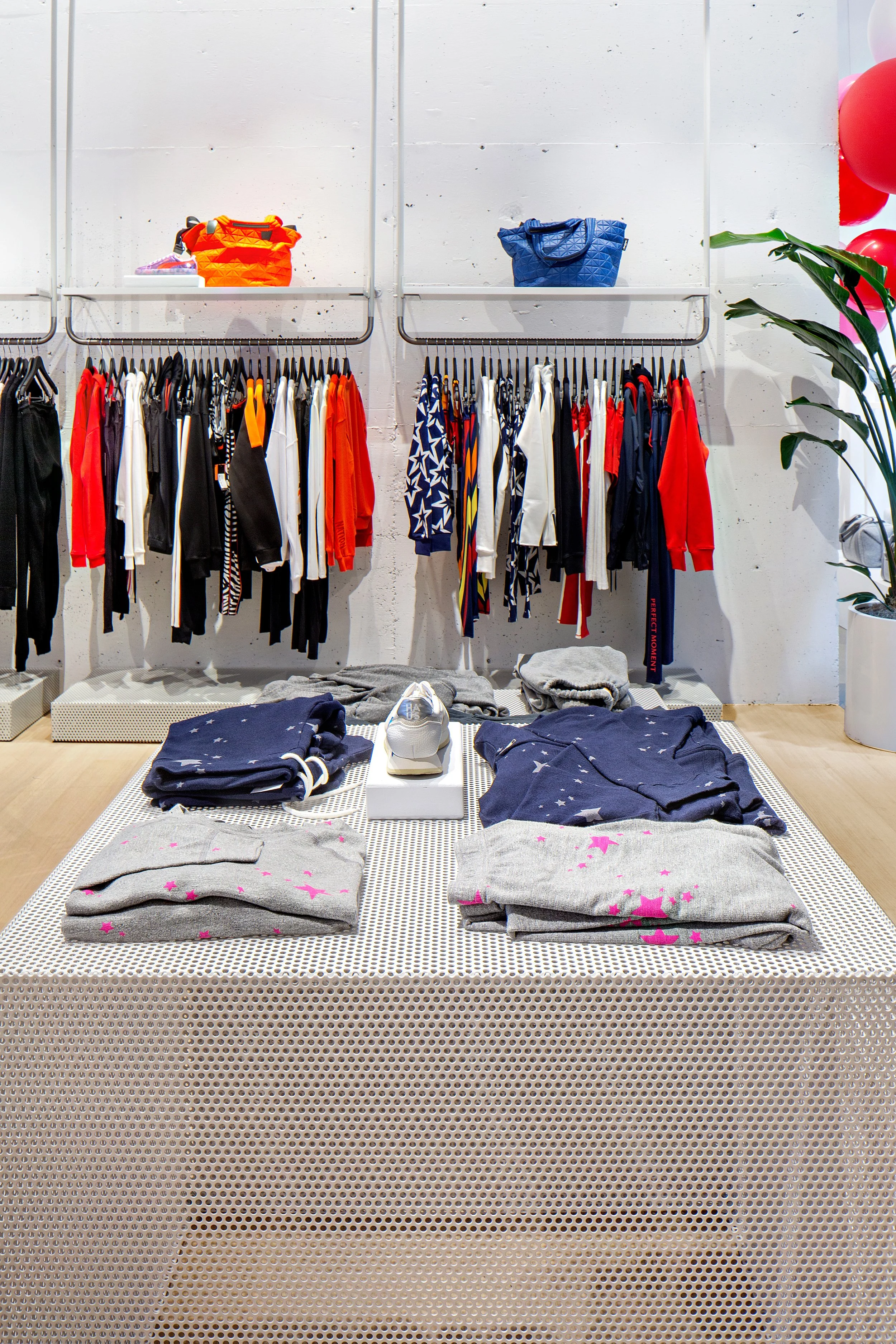 Clothing store interior with racks of colorful garments and a display table with folded clothes and a sneaker.