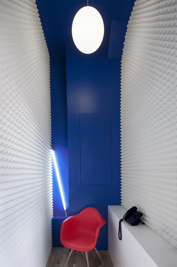 Modern minimalist room with blue walls, red chair, white textured panels, and a black phone on a ledge.